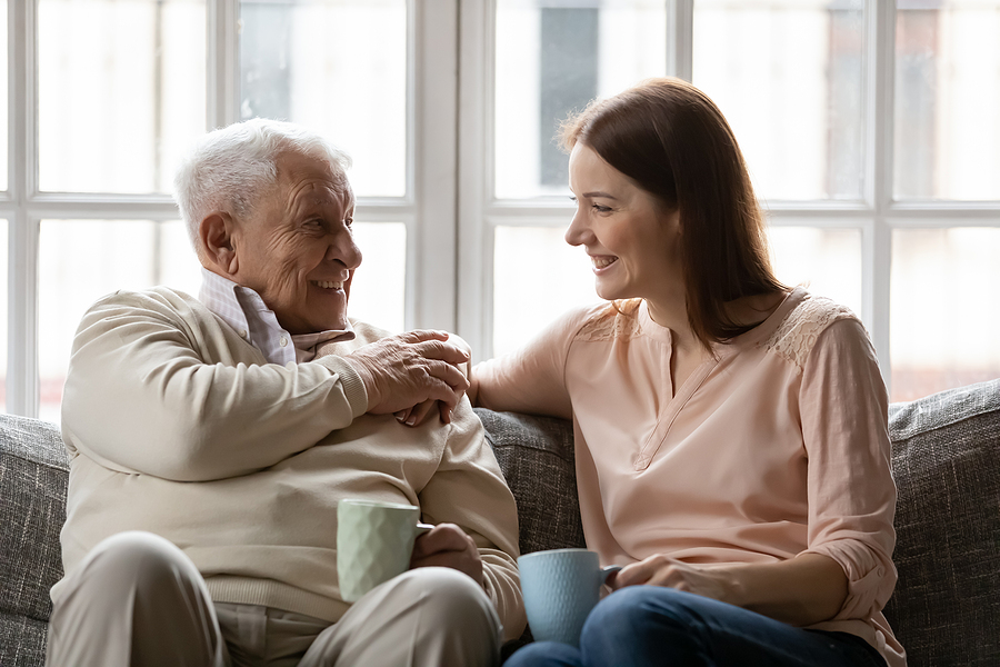 Senior and a young woman sitting together on a couch with a cup of coffee