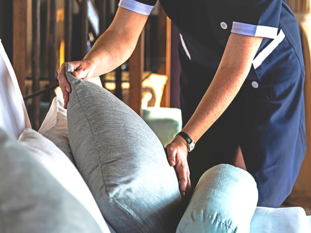 A worker in blue clothing adjusting the pillow of a couch