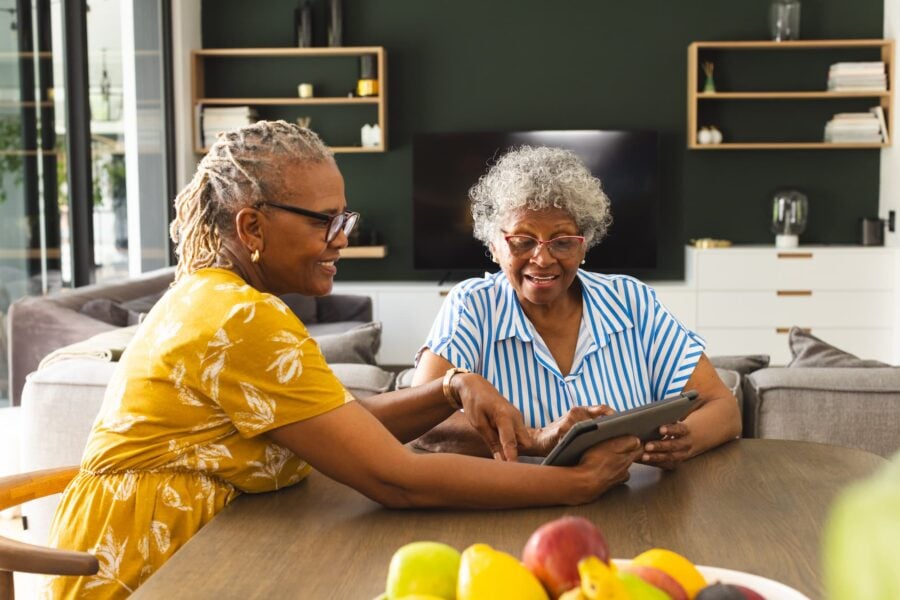 Two senior woman smiling at a dining table, holding an IPad as they review senior living options
